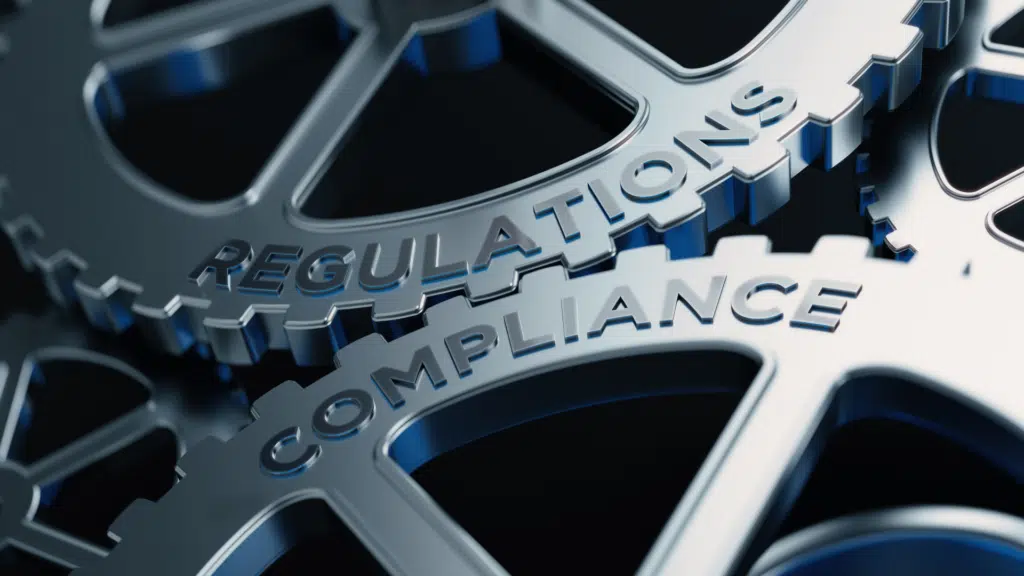 Two gears interlocking; one with the label "regulations" and the other "compliance".